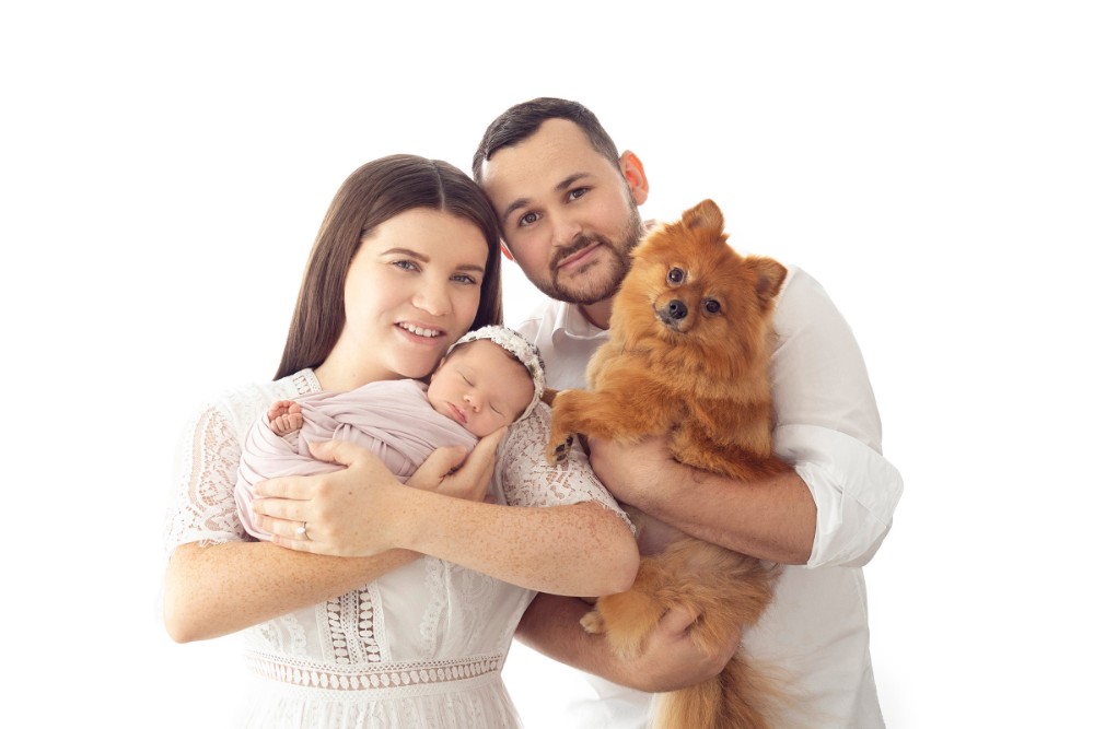 New parents holding swaddled baby girl with their dog, bright family portrait in Essex studio