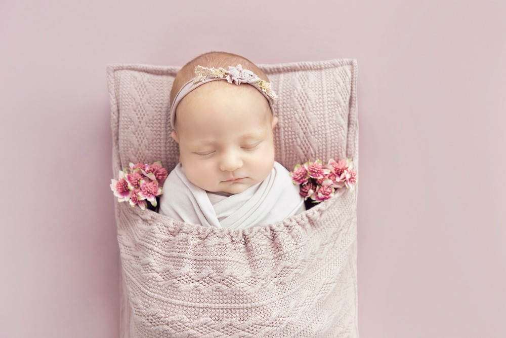 Sleeping newborn girl wrapped in pastel pink with flowers in a cosy setup, styled in Brentwood, Essex