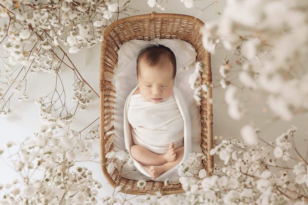 Peaceful baby in wicker basket surrounded by soft white flowers, natural Essex newborn photography