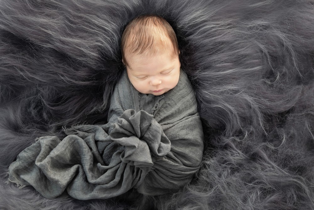 Sleeping newborn in grey wrap on fluffy fur, elegant Essex baby portrait session