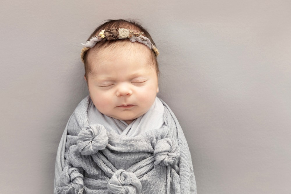 Newborn girl in grey wrap with floral headband, adorable Essex sleeping baby photography