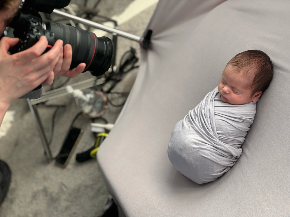 Behind-the-scenes Essex newborn photoshoot, photographer styling swaddled baby boy in grey