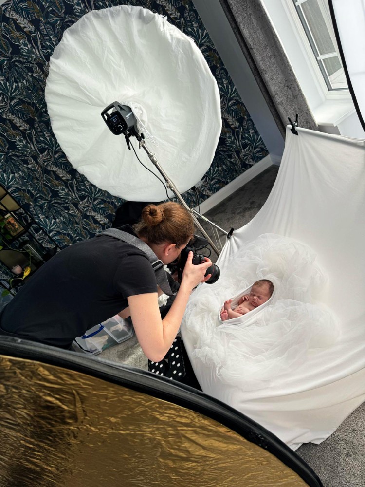Photographer capturing swaddled newborn in white tulle with softbox, Essex studio session