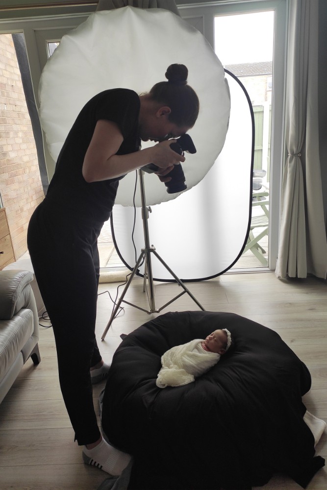 Photographer capturing swaddled newborn on black beanbag with softbox, pro Essex baby session