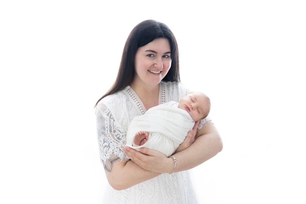 Mother in white lace holding sleeping newborn in bright Essex studio portrait
