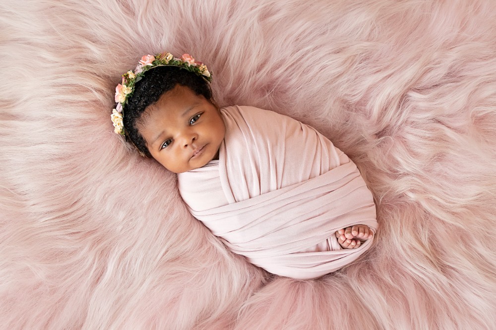 Newborn baby girl with floral headband, swaddled on pink fur, Essex precious portrait