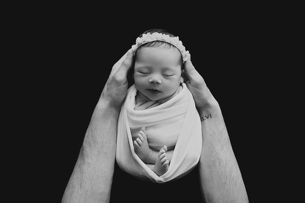 Black-and-white swaddled newborn in father’s hands, precious Essex baby face portrait