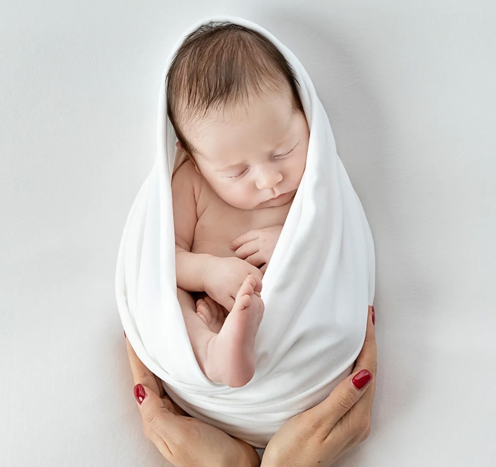 Swaddled newborn in mother’s hands on white backdrop, timeless Essex baby photography session