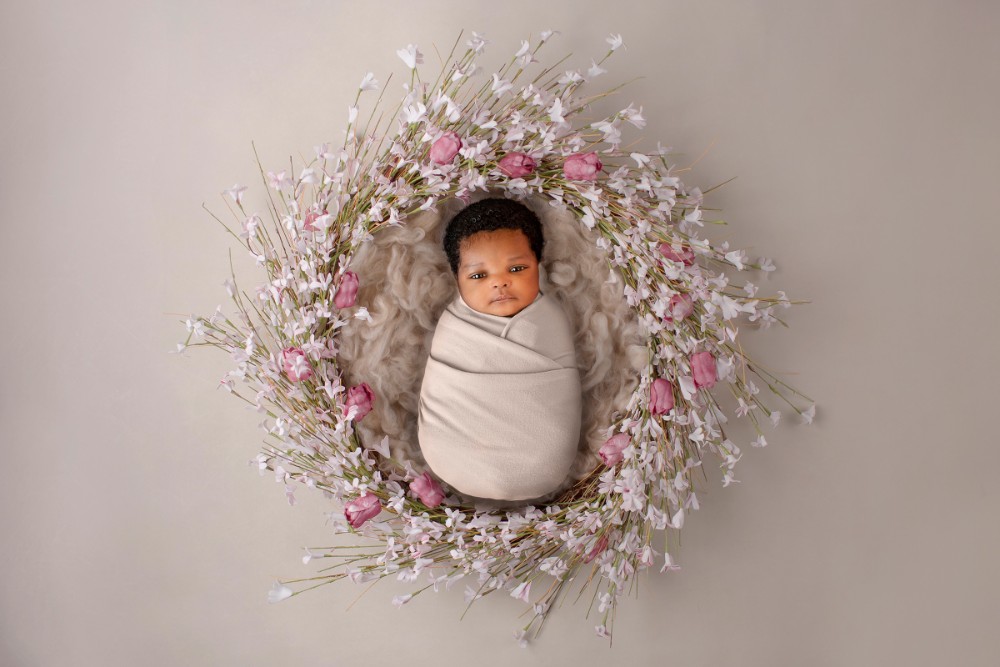 Wide-awake newborn in cream wrap nestled in pink floral wreath, enchanting Essex baby portrait