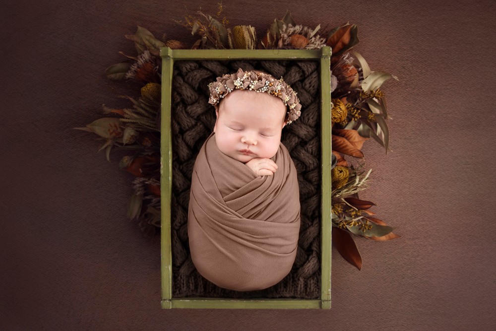 Baby girl sleeping in an earthy crate with floral headband, cosy autumn newborn portrait in Essex
