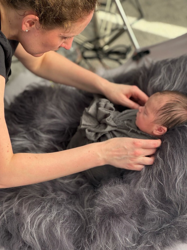 Photographer styling newborn in grey wrap on fur backdrop, professional Essex photoshoot