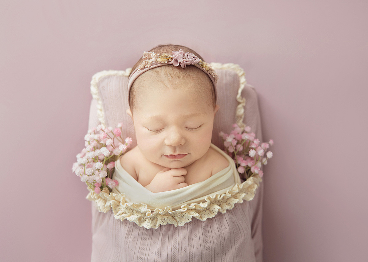 Peacefully sleeping newborn baby girl wrapped in soft fabric with a delicate headband during a newborn photoshoot in Brentwood Essex.