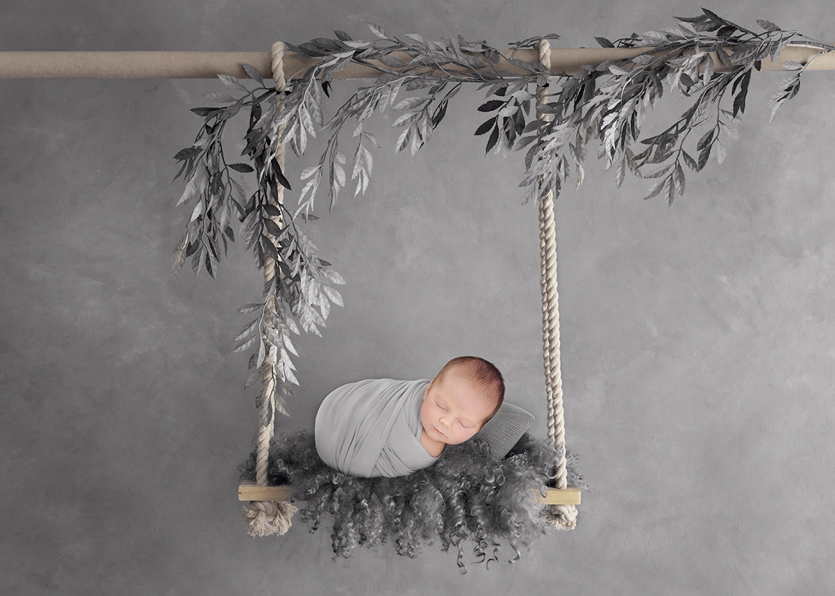 Sleeping newborn wrapped securely in a styled swing setup created using safe newborn photography techniques.