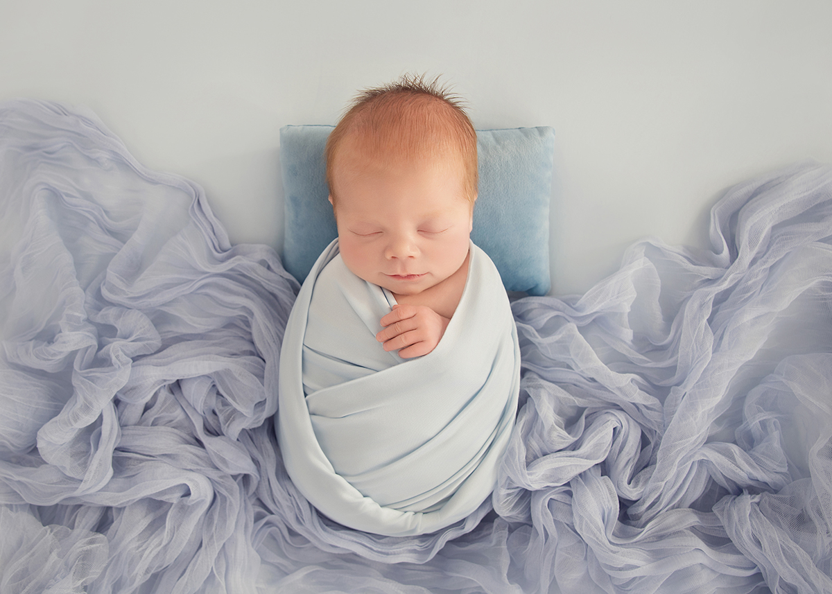 Fine art newborn baby portrait wrapped in soft blue fabric surrounded by flowing textures photographed during newborn photography session in Southend Essex.