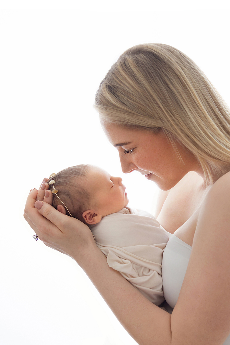 Mother gently cradling her sleeping newborn during a calm baby-led newborn photography session.