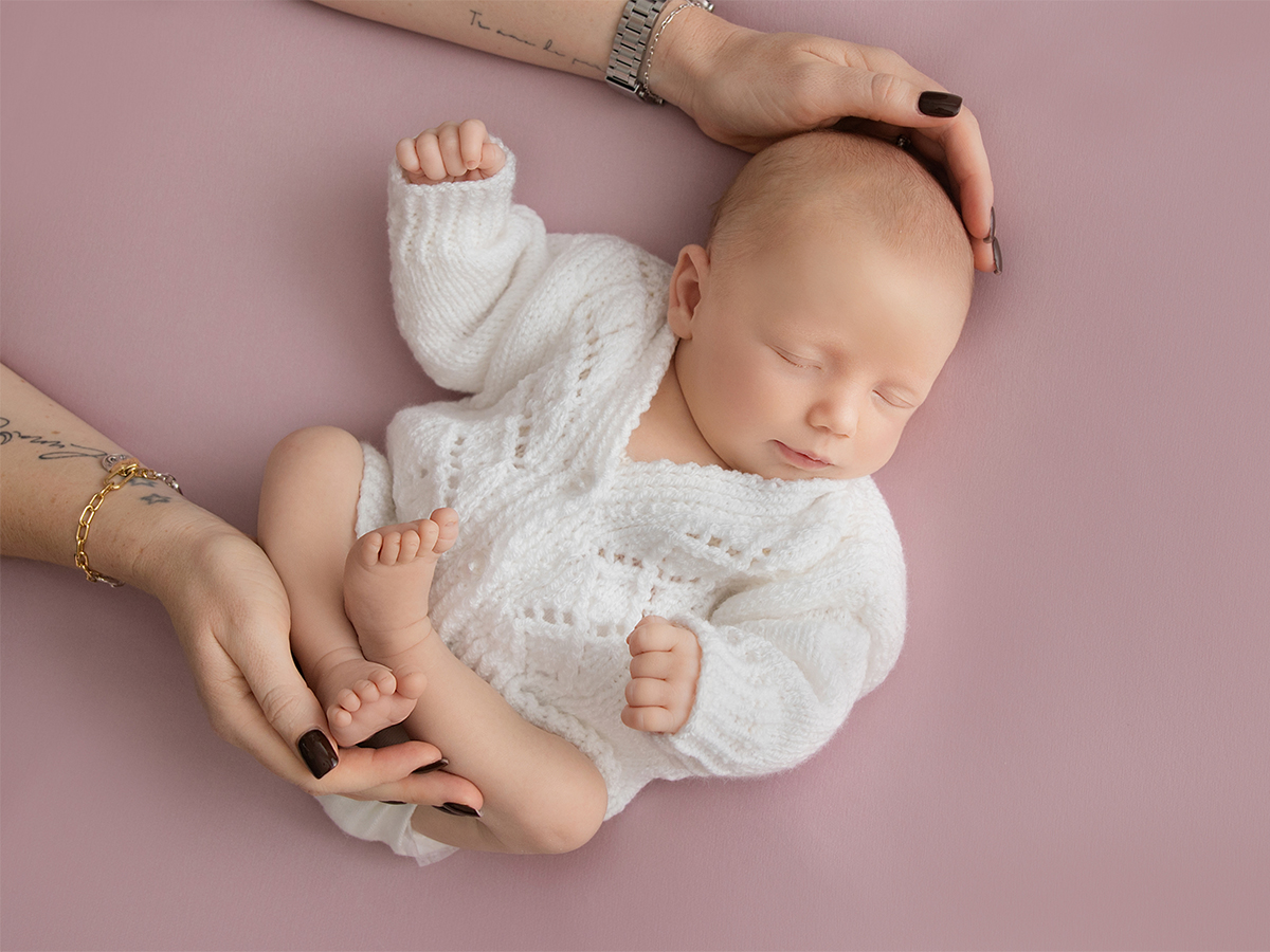 Natural newborn baby portrait in soft knitted outfit with gentle parent hands supporting baby during professional newborn photography session in Tiptree Essex.