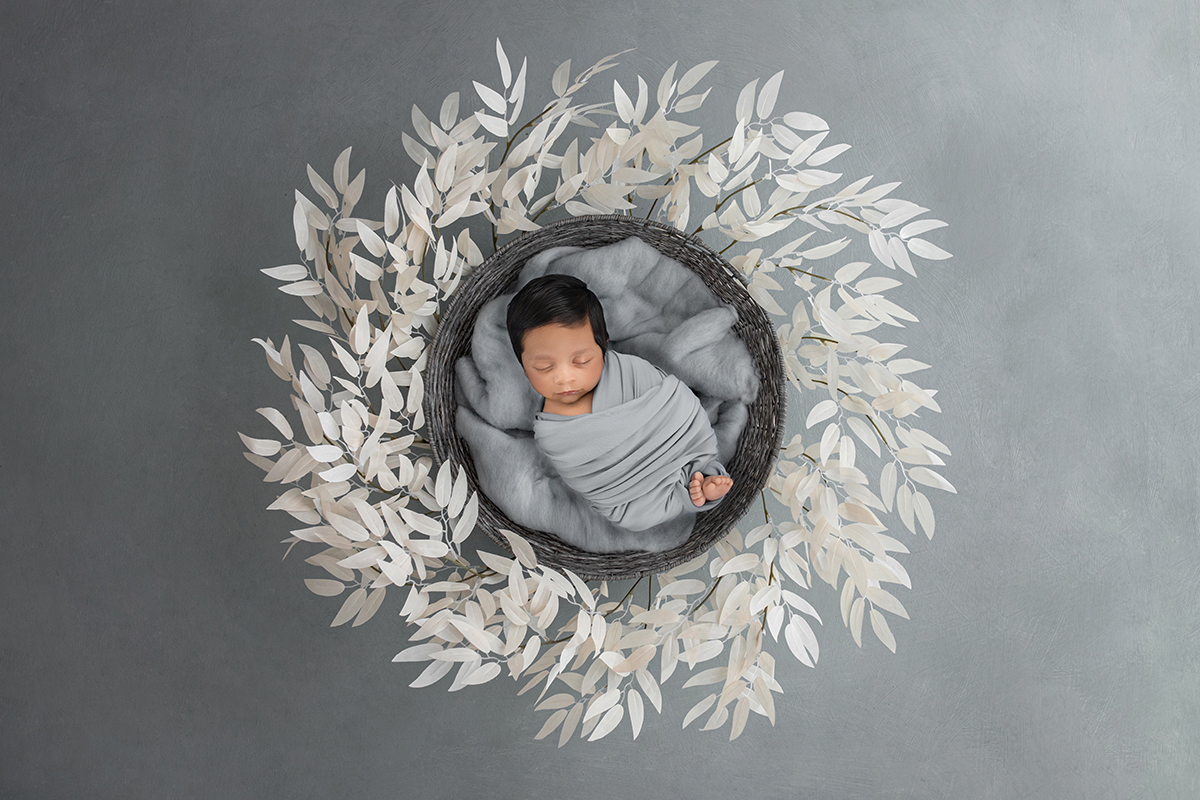 Peaceful newborn baby sleeping in soft neutral basket surrounded by textured leaves during artistic newborn photography session in Wickford Essex.