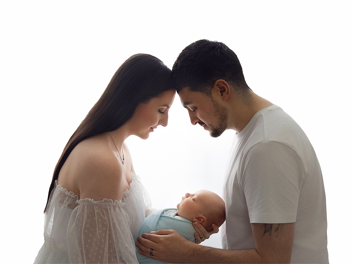 Parents wearing coordinated neutral clothing while holding their sleeping newborn during an in-home photography session.