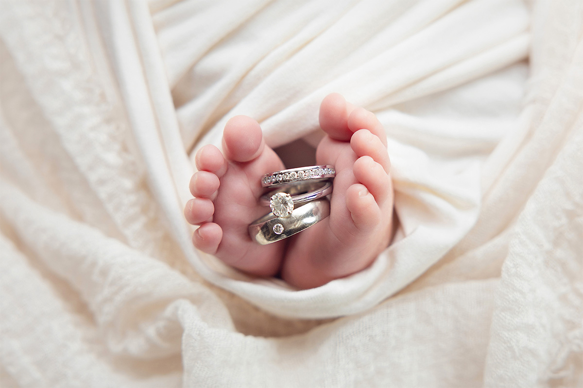Close-up newborn baby feet holding parents' wedding rings during a newborn photography session in Billericay Essex, photographed by a professional Essex newborn photographer.