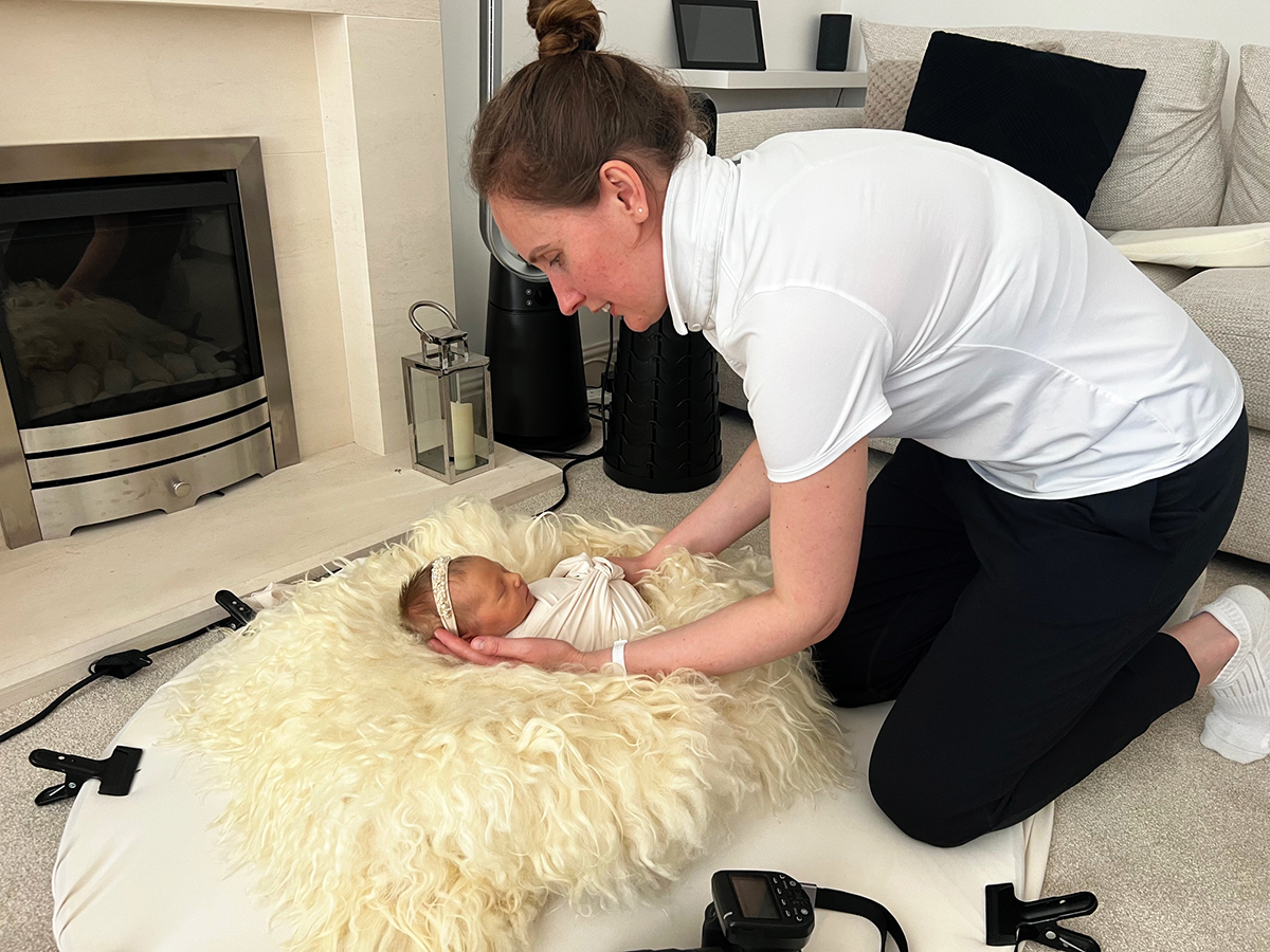 Professional newborn photographer gently supporting and positioning a sleeping baby during an in-home session.