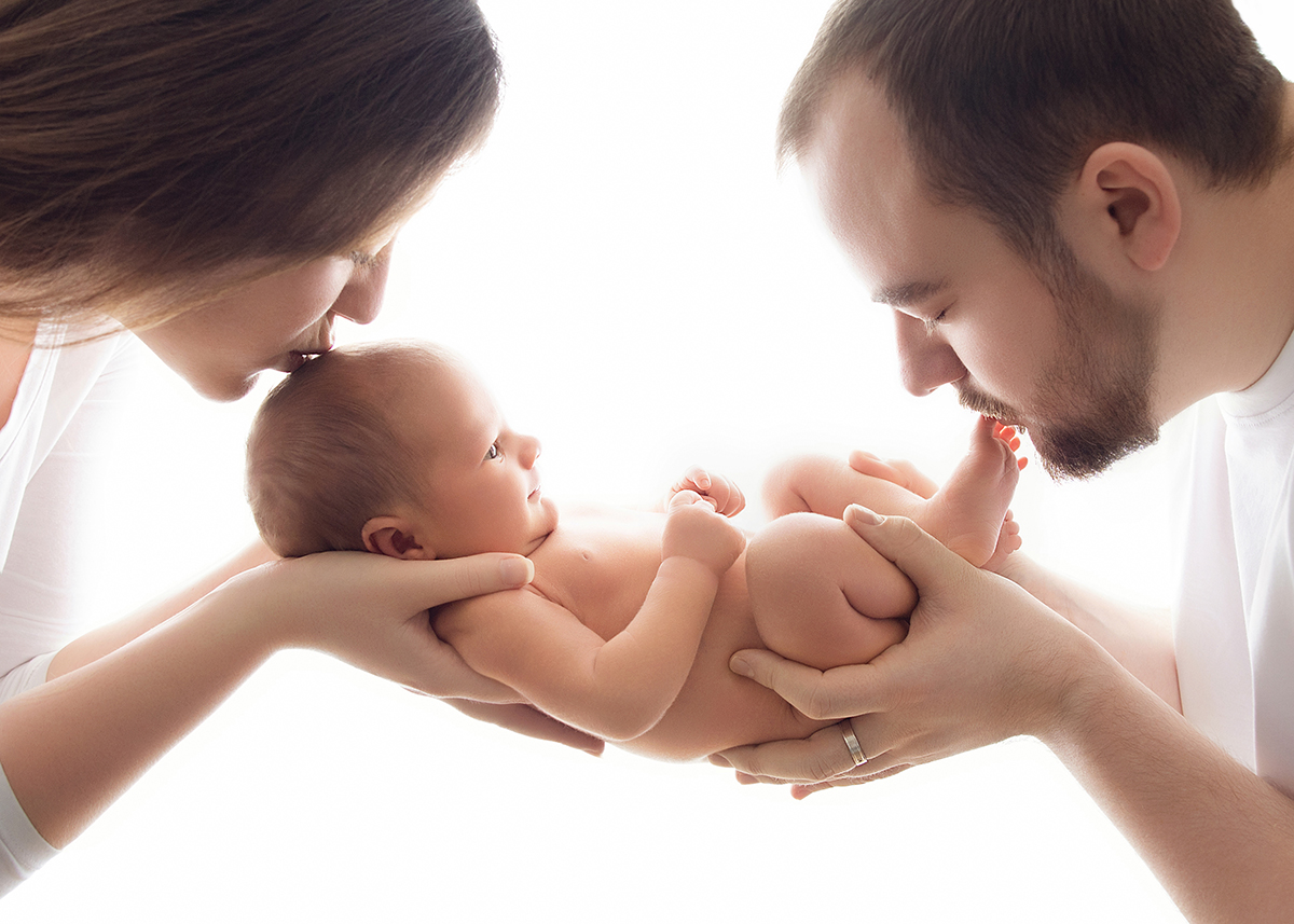 Parents gently kissing their newborn baby during emotional family newborn photography session in Brentwood Essex.