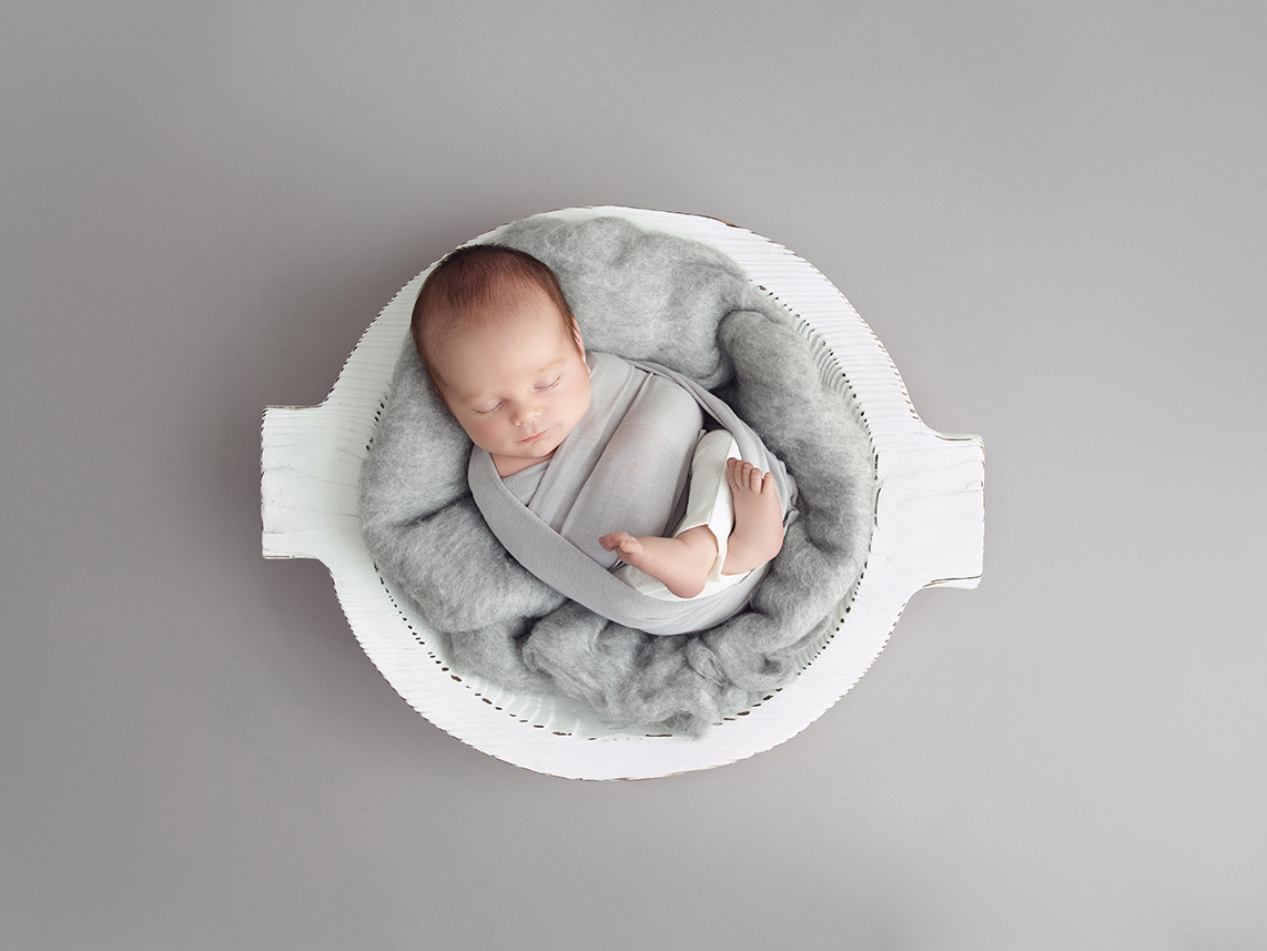 Sleeping newborn positioned safely and comfortably in a padded photography bowl with continuous support nearby.