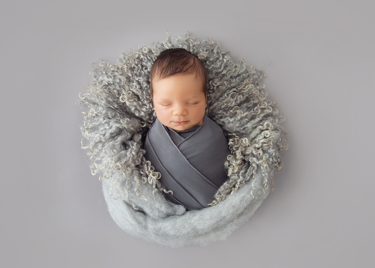 Sleeping newborn safely wrapped in soft grey fabric during a professional newborn photography session.