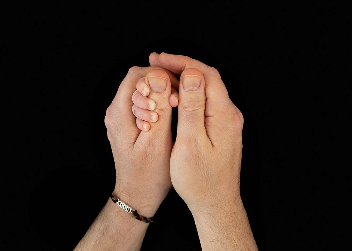 Close-up newborn baby hand gently held between a father’s hands during an intimate newborn photography session in Maldon Essex.