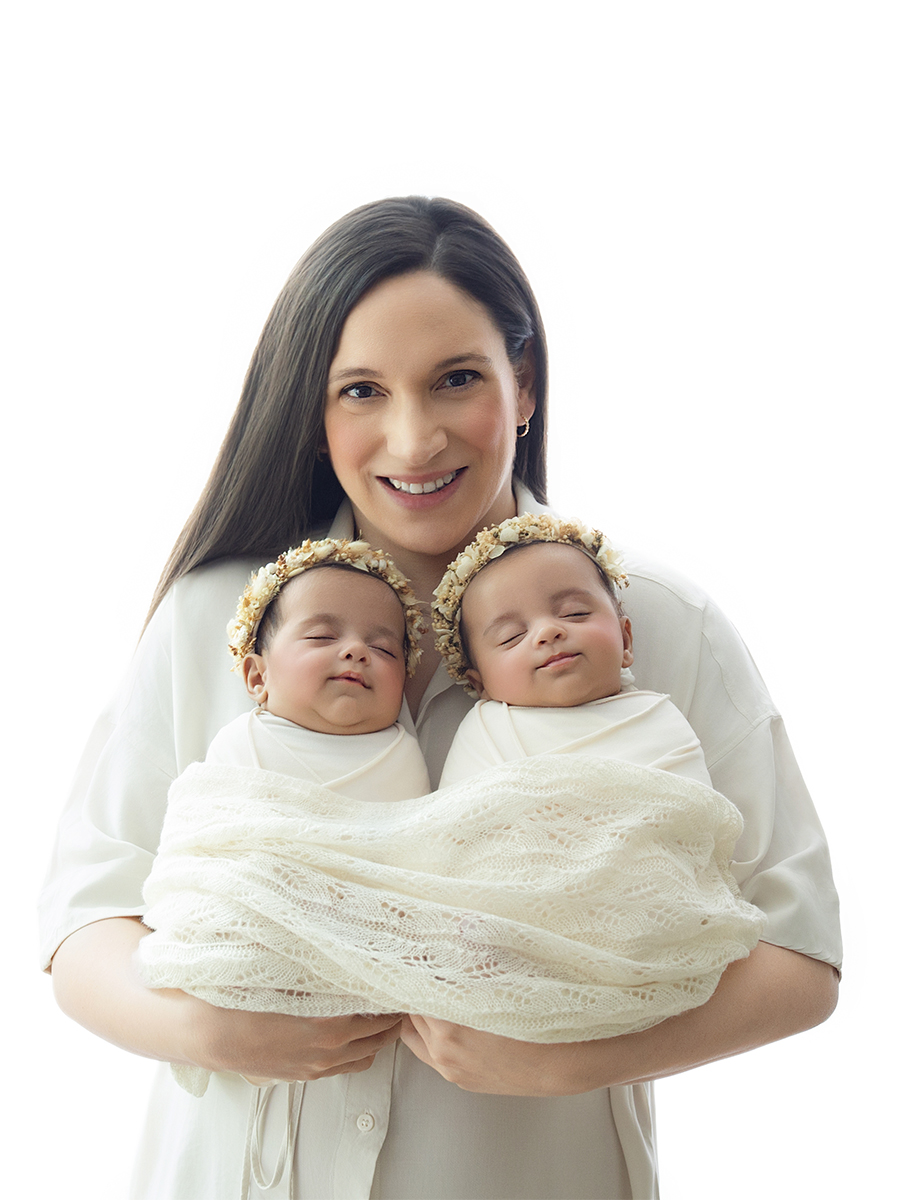Mother holding her newborn twins wrapped in soft neutral blankets during an in-home photography session.