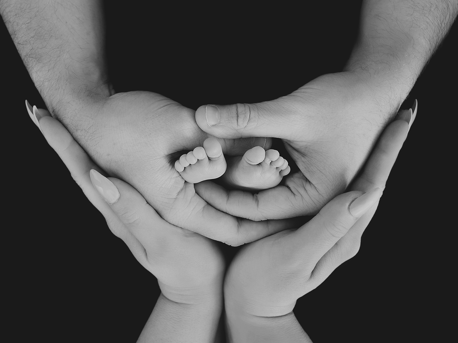 Artistic black and white photo of newborn baby feet cradled by parents’ hands, symbolising love and connection.