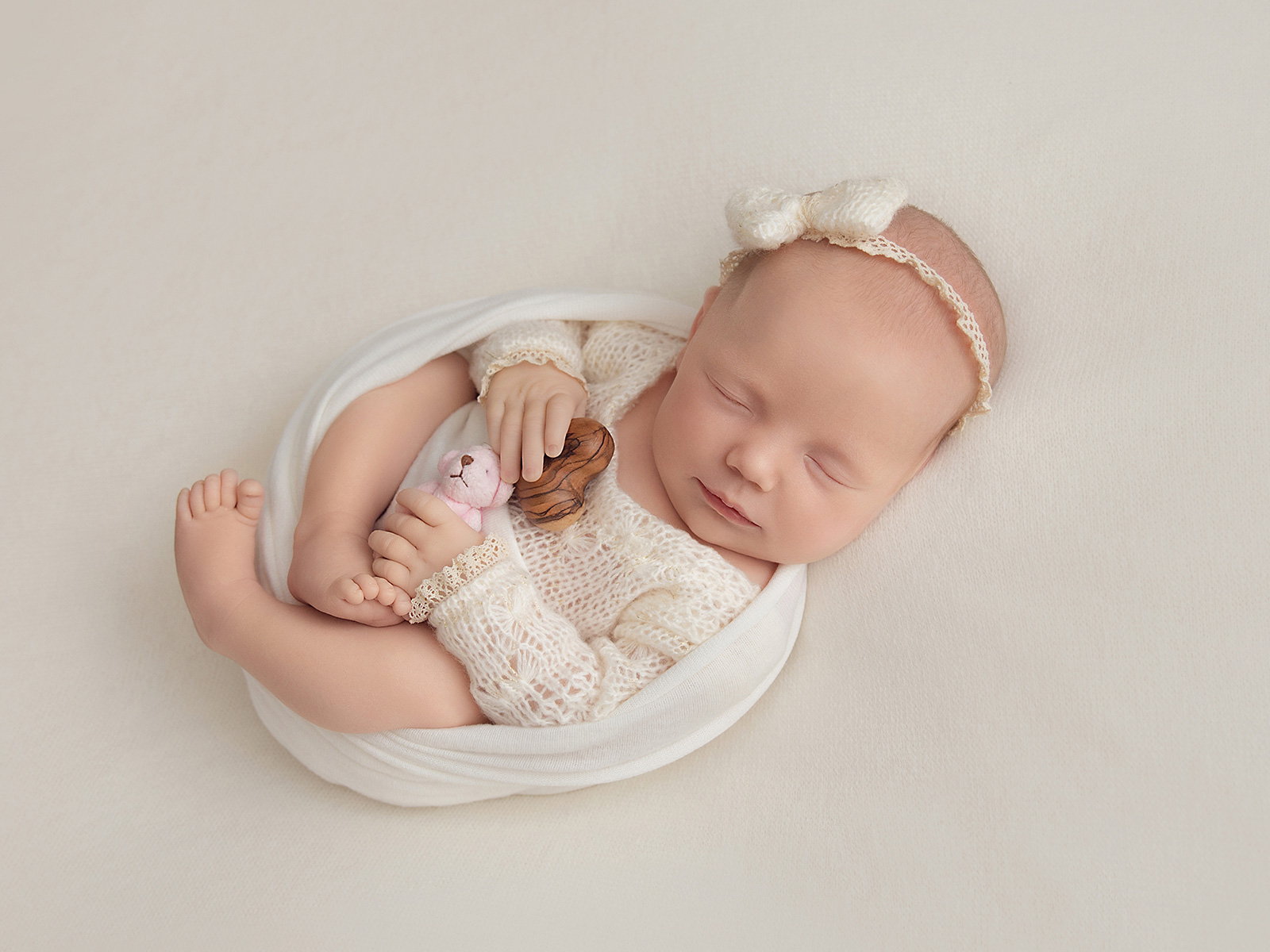 Peaceful newborn baby girl swaddled in cream, cuddling soft teddies, captured in a professional home newborn session in Essex.