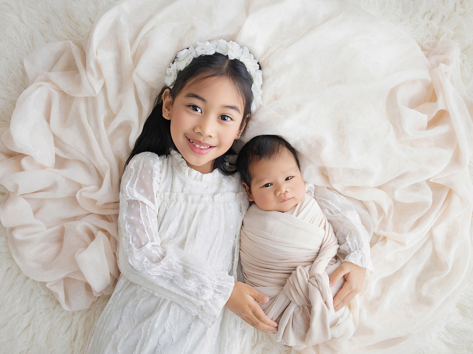 Loving big sister cuddling her newborn baby brother, photographed at home on soft cream blankets in Essex.